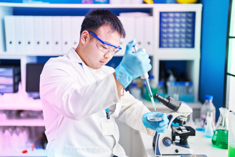 A man in a lab coat uses a pipette while conducting an experiment in a laboratory setting.