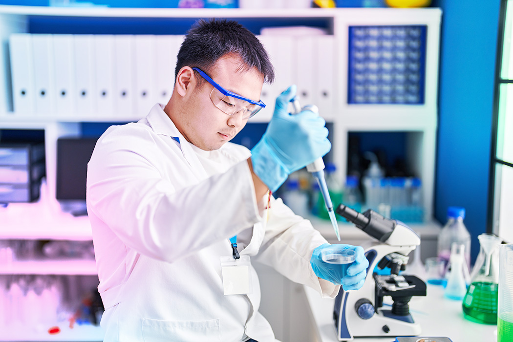A man in a lab coat uses a pipette while conducting an experiment in a laboratory setting.